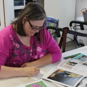 A woman wearing a pink shirt and glasses looking at a book of artwork