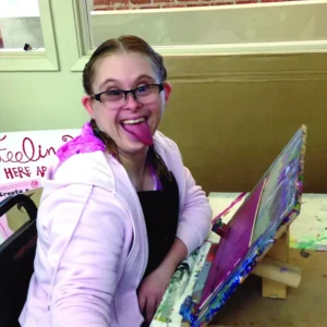 A woman wearing glasses and sticking out her tongue while smiling at the camera